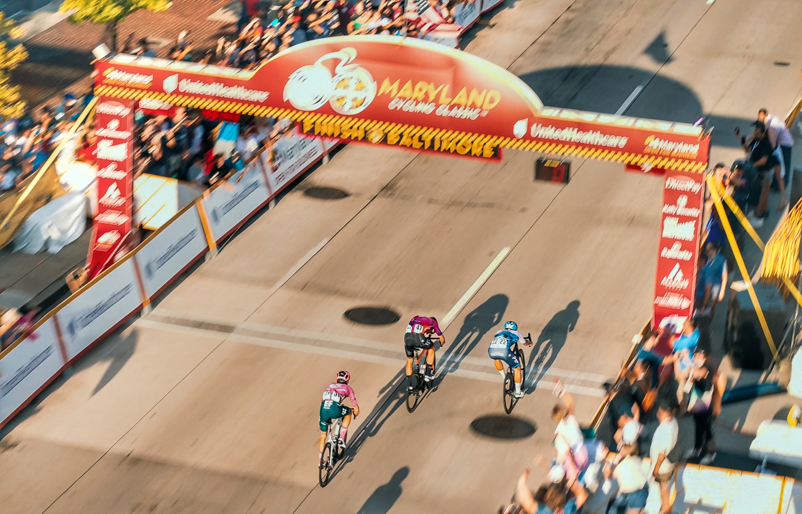 Cyclists crossing the finish line at the Maryland Cycling Classic in Baltimore, seen from above.